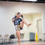 Woman practicing a Muay Thai knee strike in a training room.