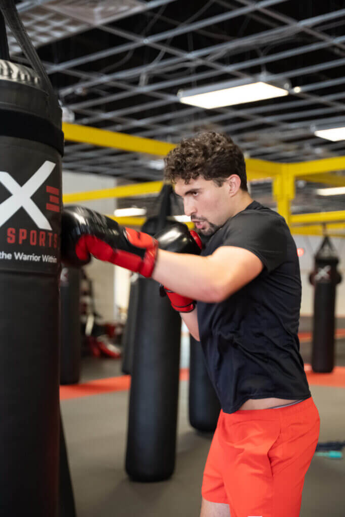 Picture of man practicing boxing self defense moves with a heavy bag at X3 Sports.