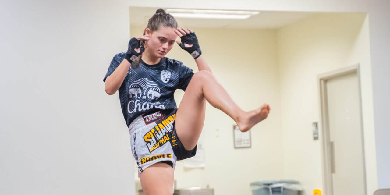 Woman practicing a Muay Thai knee strike in a training room.