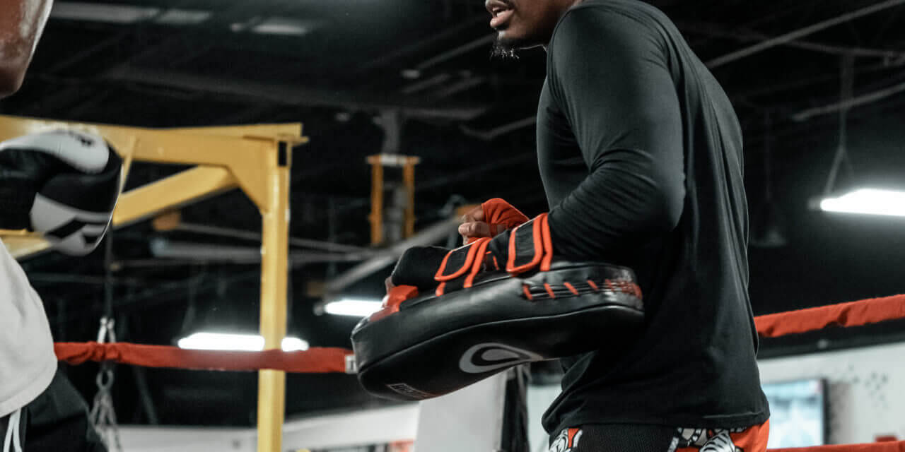 Male Muay Thai trainer holding pads during a training session.